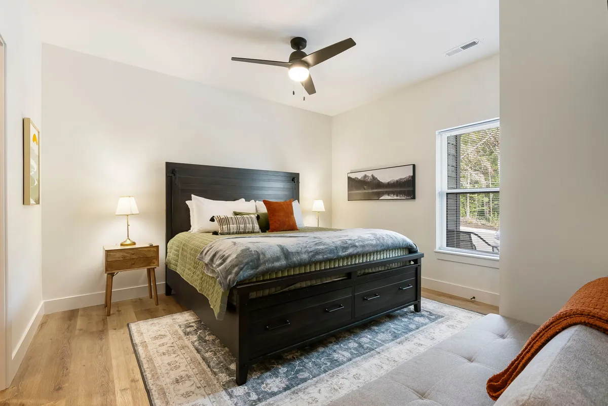 A tranquil bedroom featuring a neatly made bed with cozy, textured bedding, a nightstand topped with a lamp, and a window letting in abundant natural light. The space feels restful, bright, and perfectly suited for relaxation.