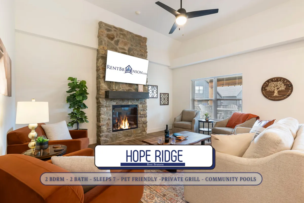 The image showcases a cozy living room featuring a striking stone fireplace, plush comfortable seating arranged for easy conversation or relaxation, and a large TV perfect for movie nights. The room exudes warmth and is ideal for gatherings, with soft lighting and inviting decor.