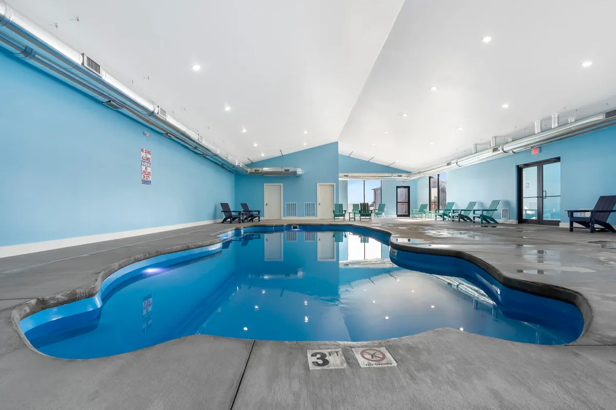 A refreshing indoor pool area with turquoise blue walls, several lounge chairs, and sparkling water. The space is tranquil and inviting, perfect for both solo relaxation and social gatherings around the pool.