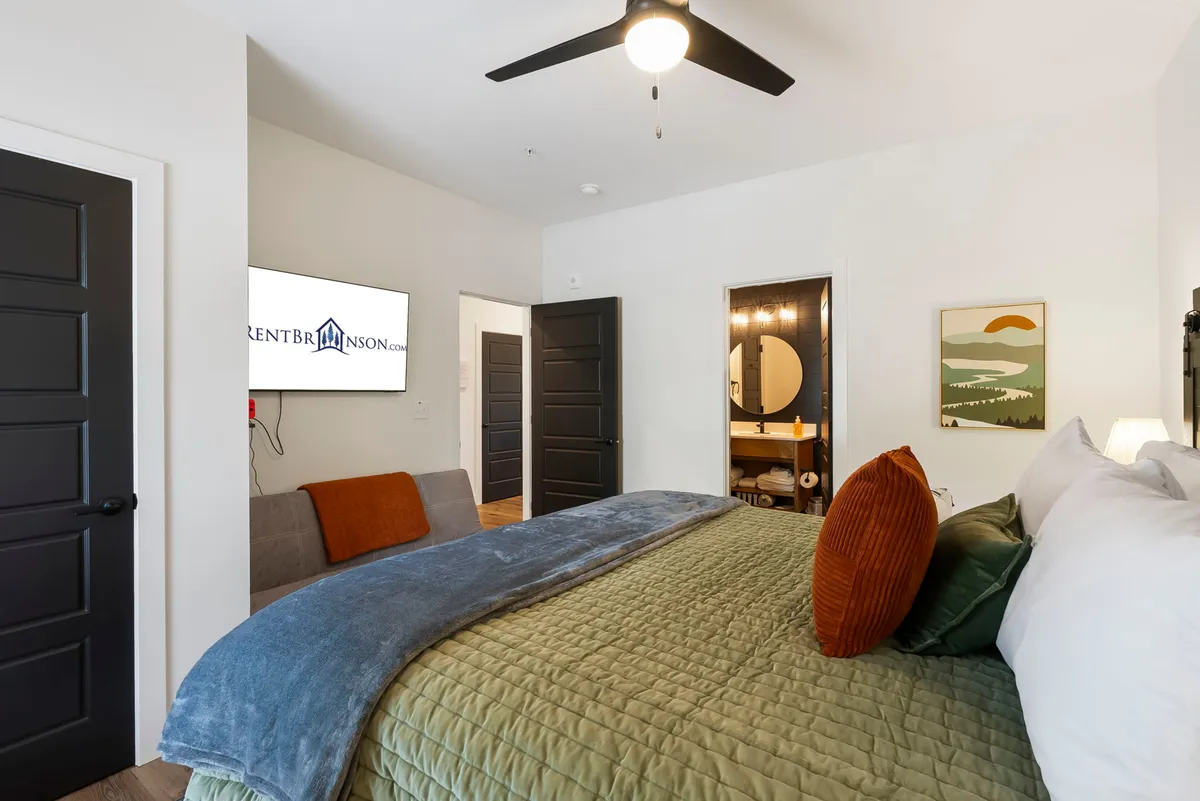 A cozy bedroom scene with a king-size bed, textured bedding, a wall-mounted television, and stylish decorative artwork. The space exudes comfort, inviting guests to unwind and enjoy both entertainment and serenity.