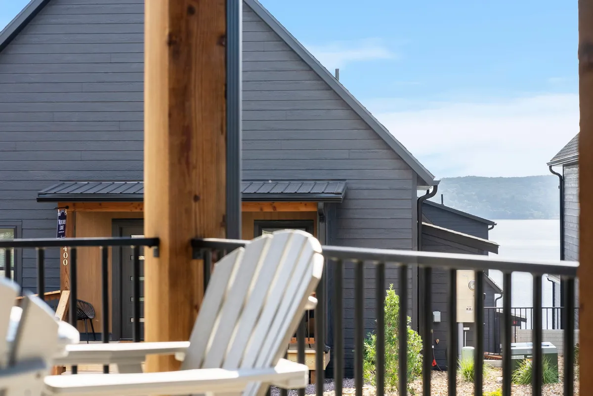 This image captures the modern architecture of the homes, a wooden porch with chairs, and a clear, tranquil view of Table Rock Lake beyond. The setting is perfect for relaxing on the porch, socializing, or simply soaking in the peaceful lakeside environment.
