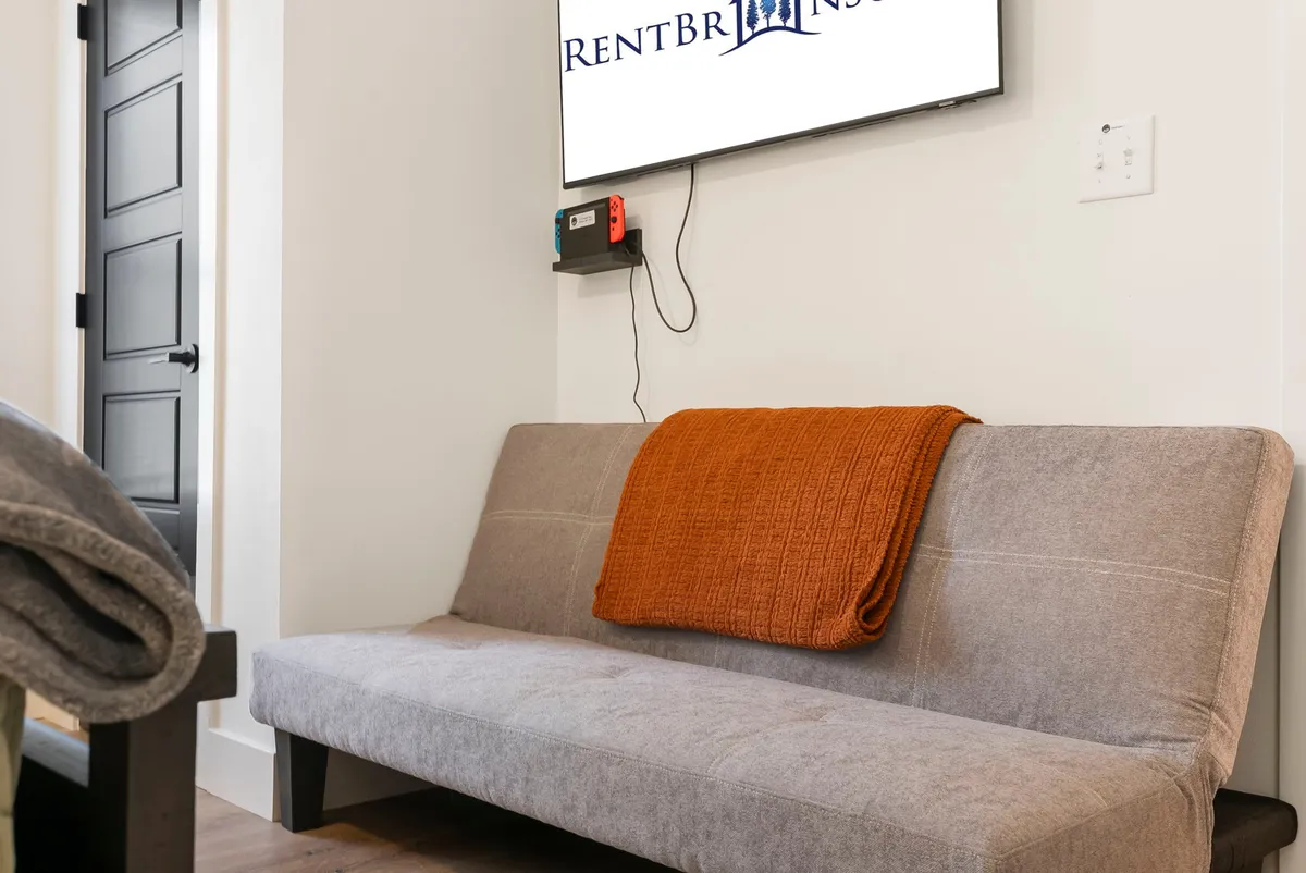A welcoming living area featuring a plush sofa draped with an orange blanket and a television, setting the stage for relaxation or transforming into a sleeping area for extra guests. The mood is cozy and family-friendly.
