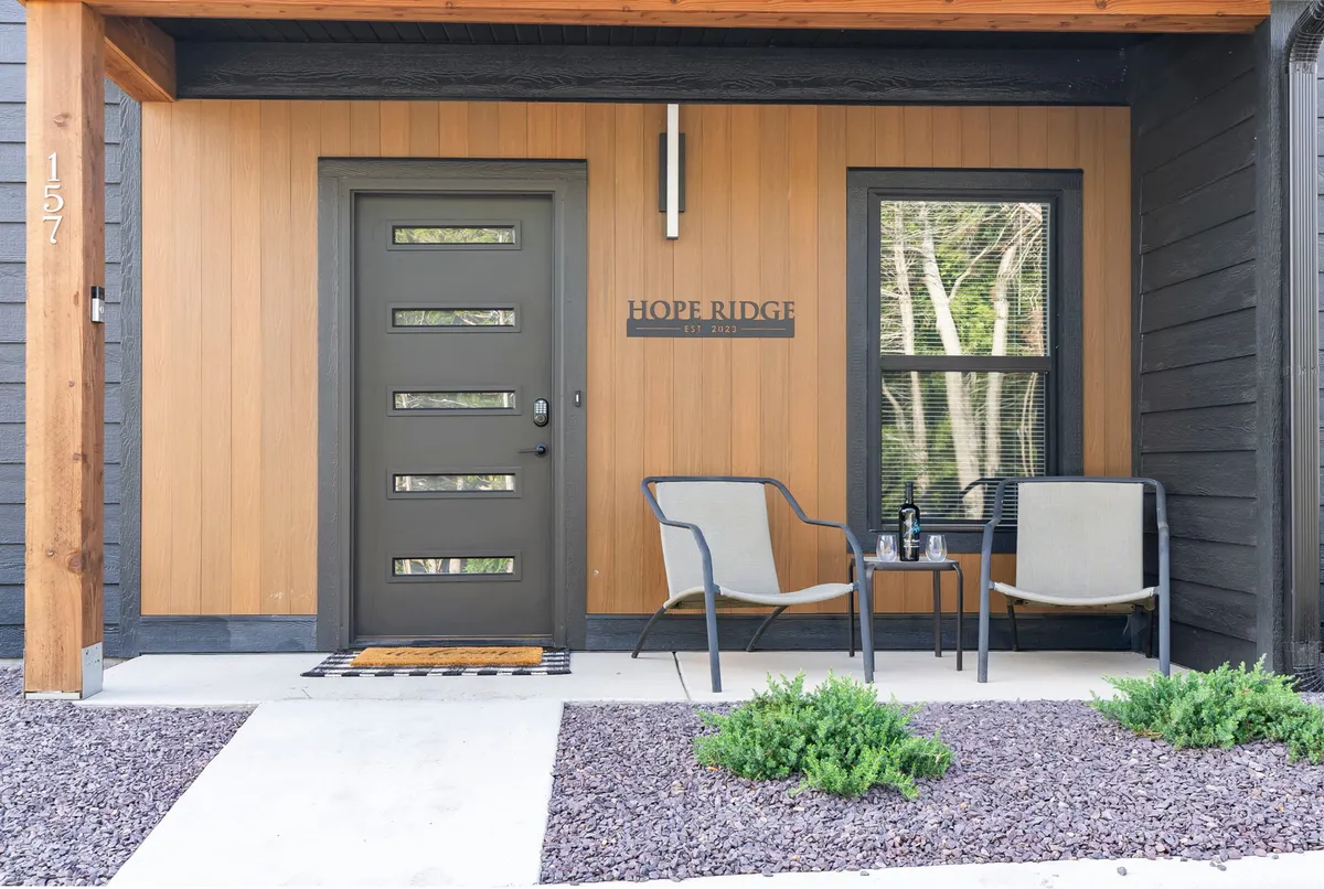 The image showcases a welcoming front door framed by a seating area and a house sign, suggesting a friendly, home-like atmosphere. The space is ideal for relaxing, enjoying a coffee, or casually watching the neighborhood go by—activities easily shared with a pet.