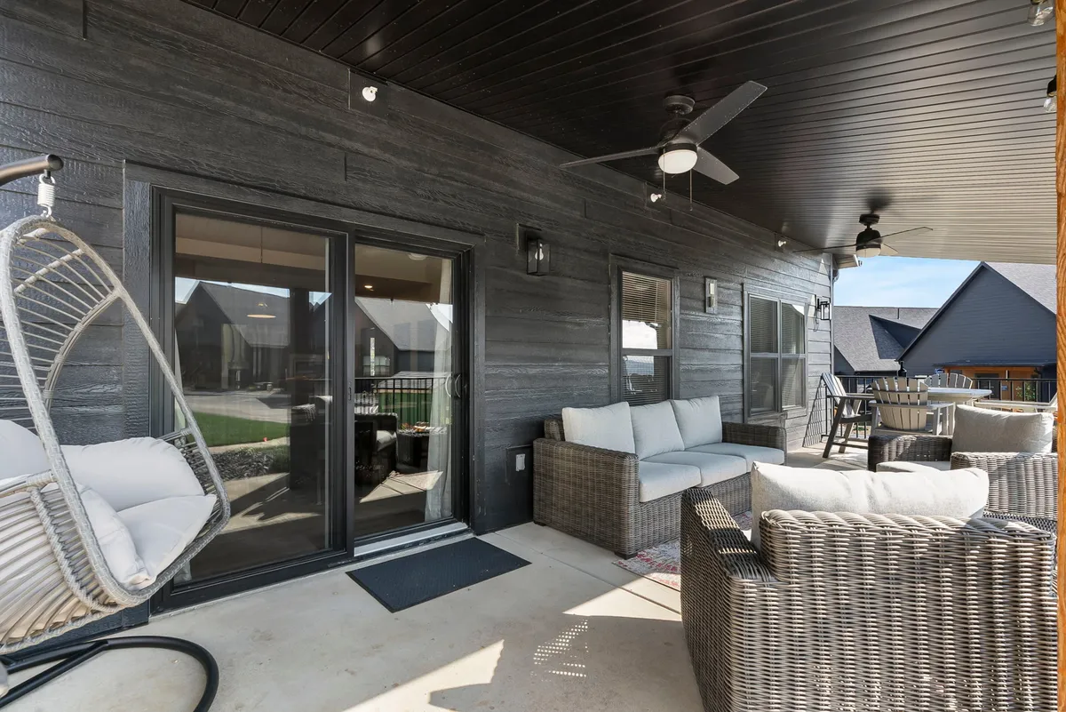 This image showcases a patio with a hanging chair, rattan seating, and double doors leading to the interior. The setup is cozy and inviting, perfect for relaxing, entertaining, or reading. The scene is bathed in warm, natural light, suggesting beautiful sunset views and comfortable evenings outdoors.